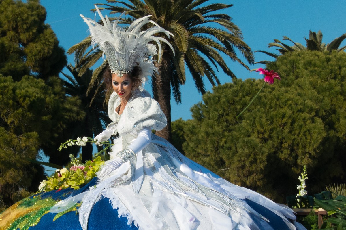 A performer in a white feathered costume throws flowers from a flower-covered float during the Battle of Flowers parade at the Nice Carnival in Nice, France