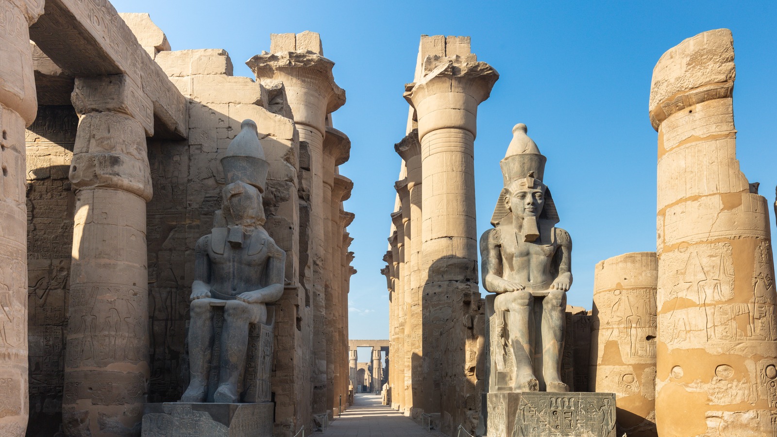 Seated statues of Ramesses II and towering columns at Luxor Temple under a clear blue sky in Luxor, Egypt.