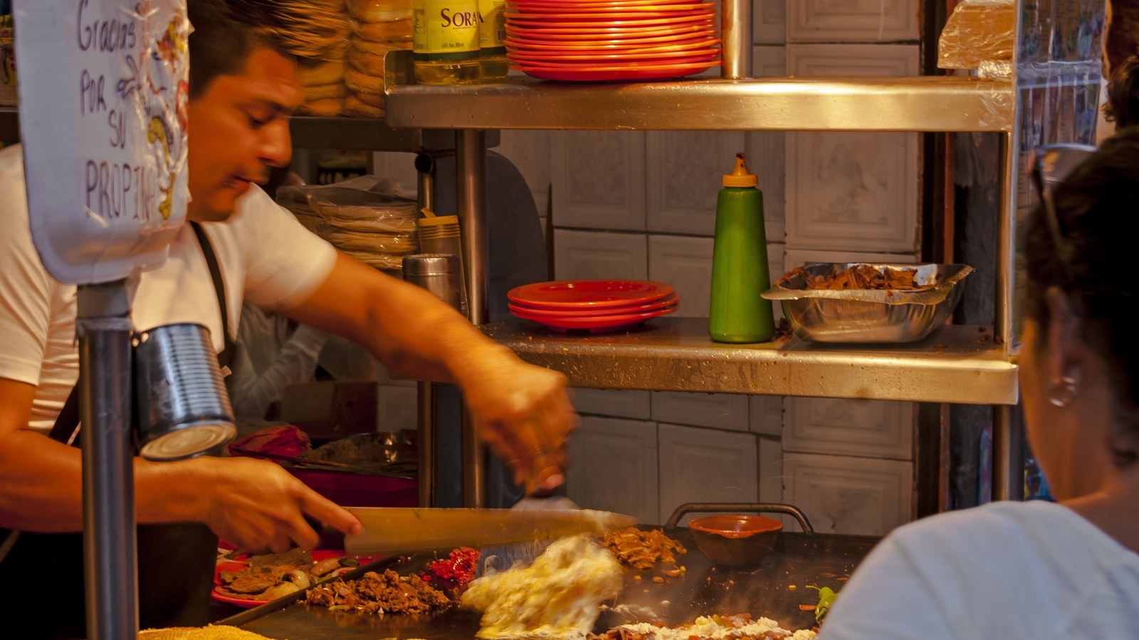 A taquero cooking chopped meat and tortillas on a steaming flat-top griddle at a street food stand in Mexico City's Centro