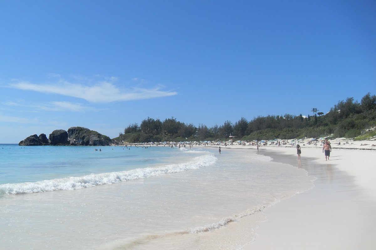 Pale pink sand and turquoise water at Horseshoe Bay in Bermuda, with rocky outcrops and visitors on the beach
