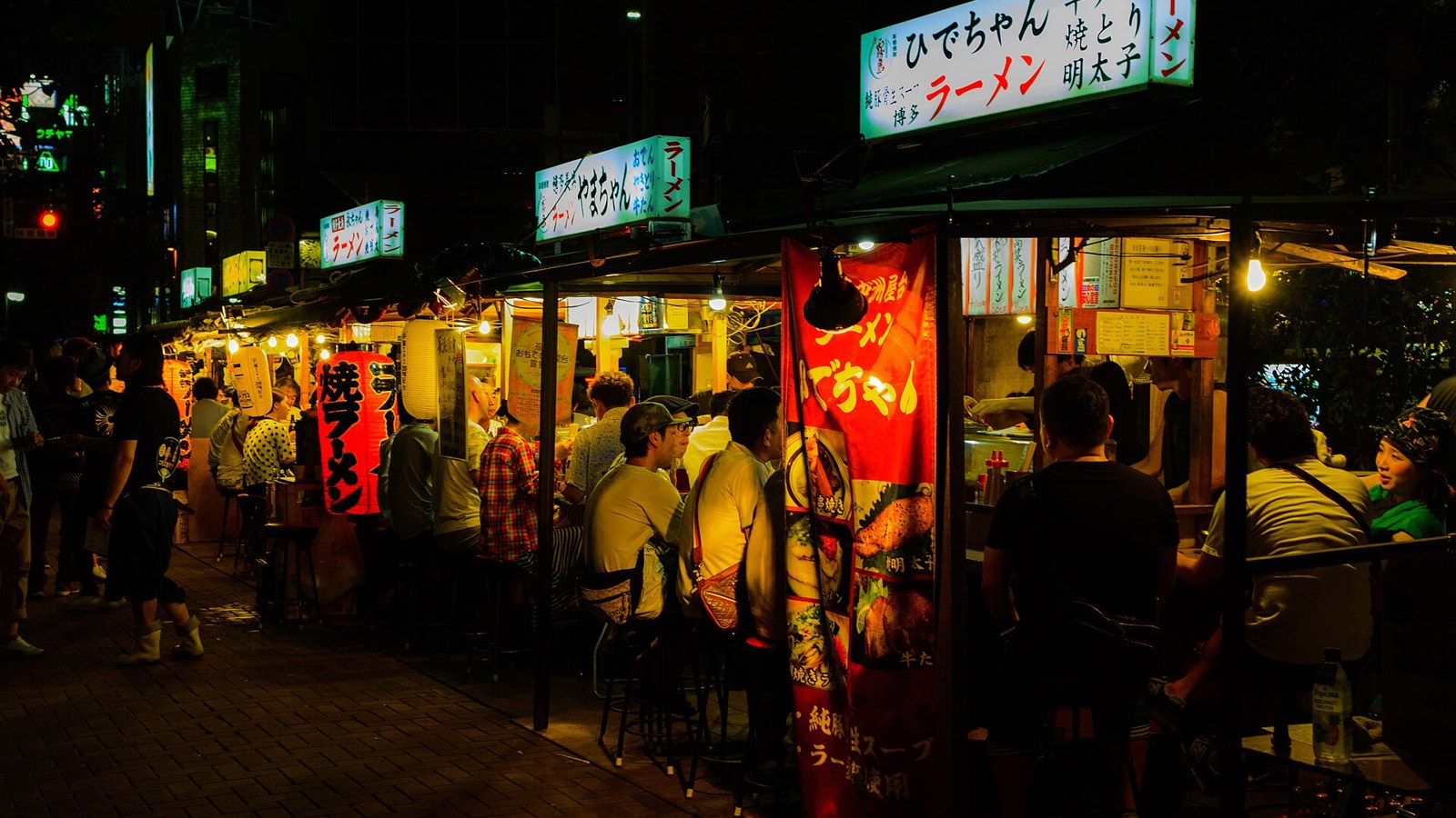 Yatai food stalls at night in Nakasu, Fukuoka, with diners eating ramen under paper lanterns