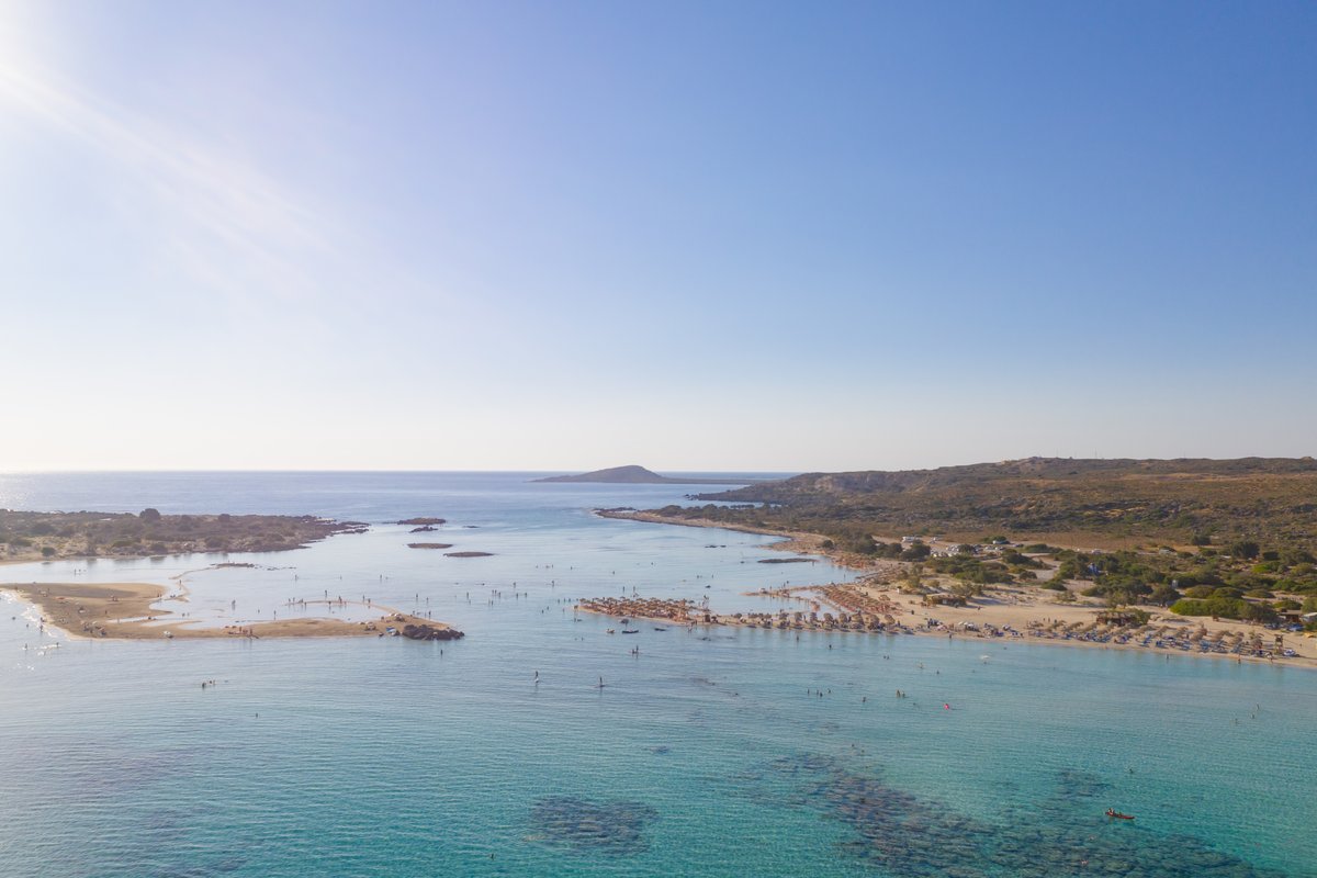 Aerial view of Elafonisi lagoon in Crete, with pink-tinged sand, turquoise water, and the sandbar islet