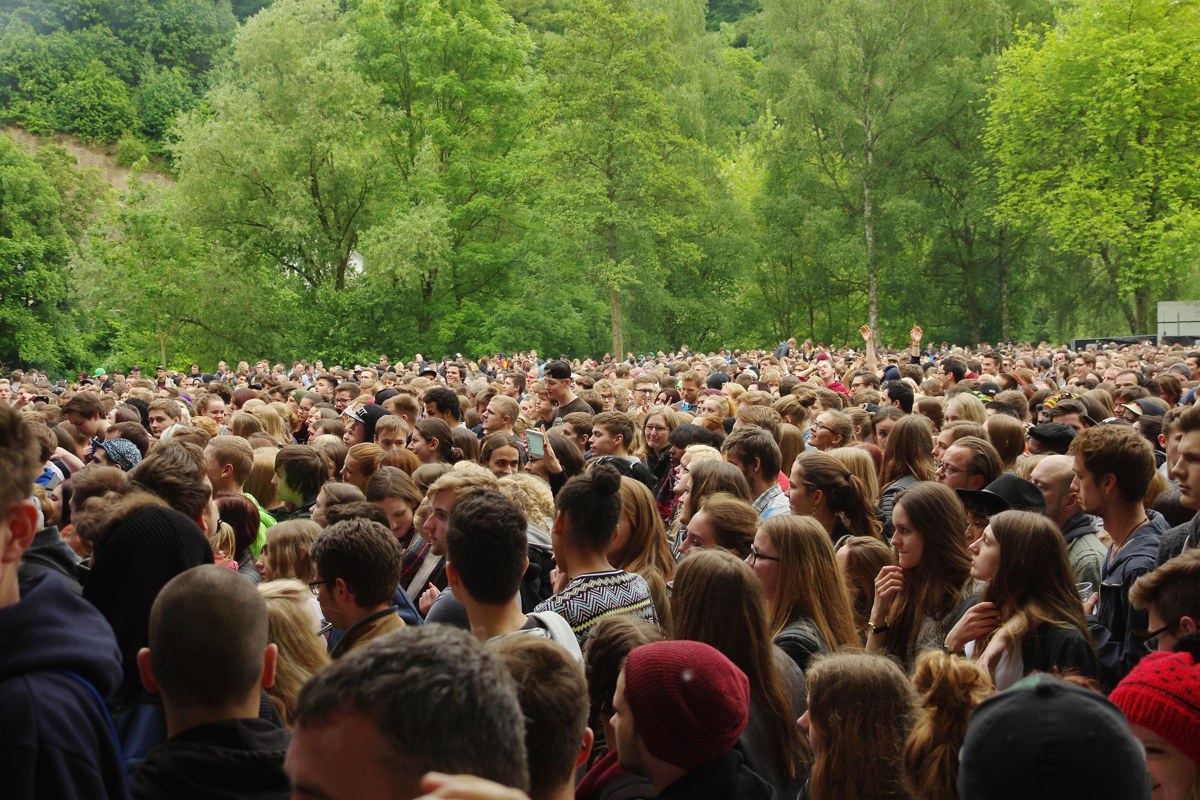 A large crowd watching an open-air music festival in a green park