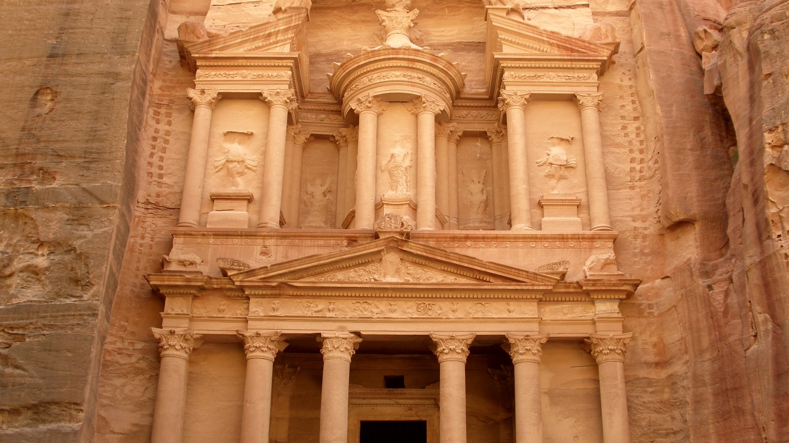 The Treasury (Al-Khazneh) at Petra in Jordan, its two-storey carved sandstone facade seen from the plaza in warm golden light